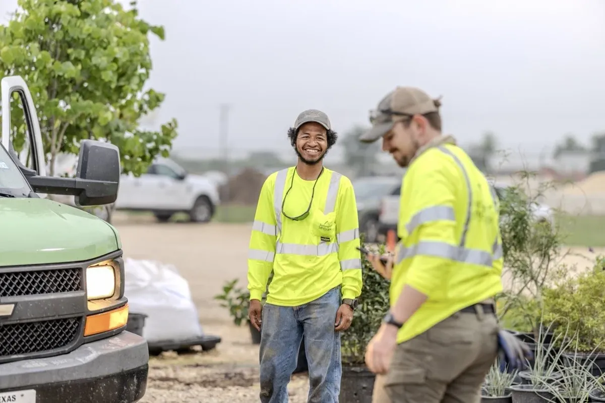 Smiling landscape crew members in high-visibility shirts at a job site